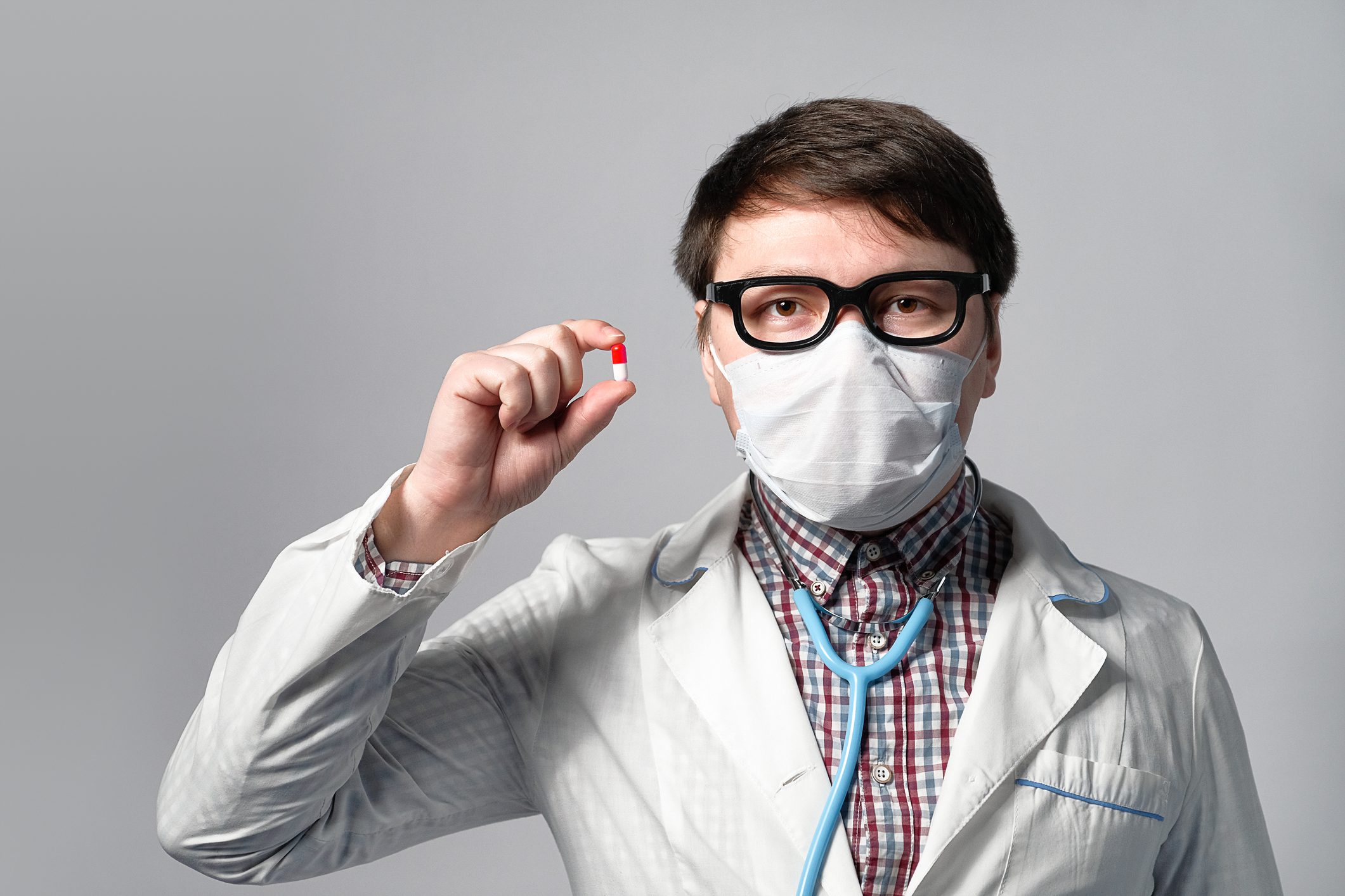 An Asian Or Chinese Doctor In A Dressing Gown And Medical Mask, Holding A Pill In His Hand . Concept Of Prevention And Treatment Of Viruses And Flu, Outbreaks Of Pneumonia And Coronavirus Epidemics.