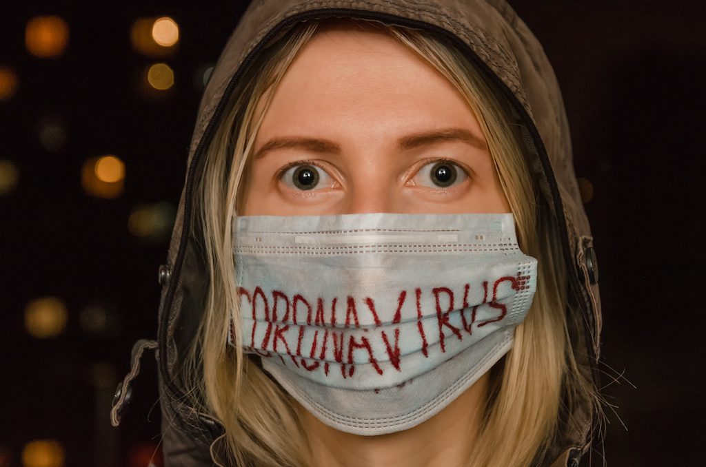 blonde girl in a hood with a medical mask on her face with the inscription coronavirus in the dark. Concept of health care, medicine