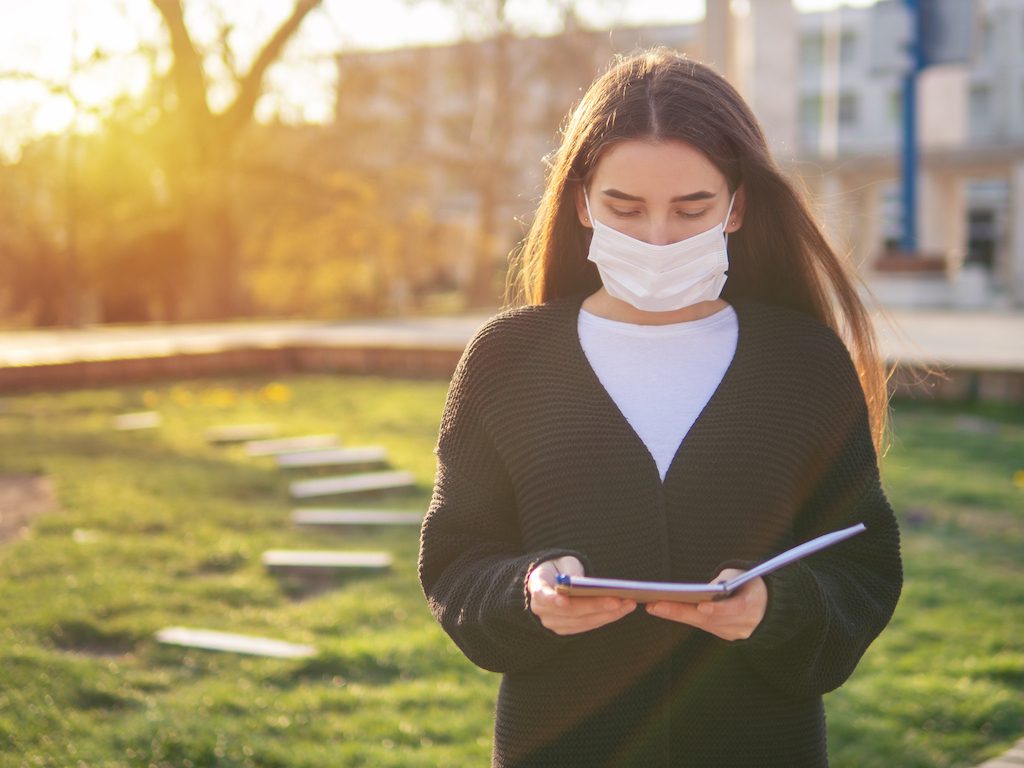 Beautiful woman in mask studying outdoors in the park, near her home. Self distancing and quarantine concept.