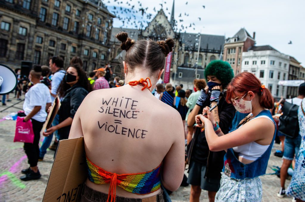 A white woman shows off her back with anti-racist writings