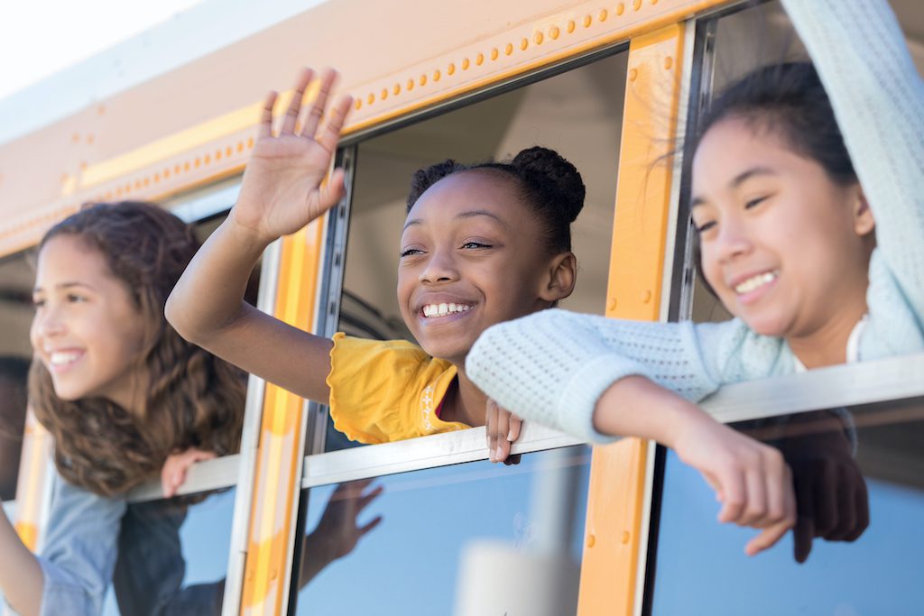 Preteen schoolgirls waving from school bus