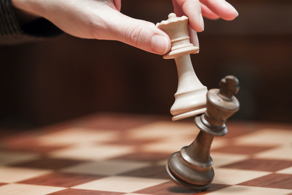 Concept: the woman who dominates the man. A woman's hand gives checkmate to the king with the queen on a wooden chessboard, with no other pieces in play