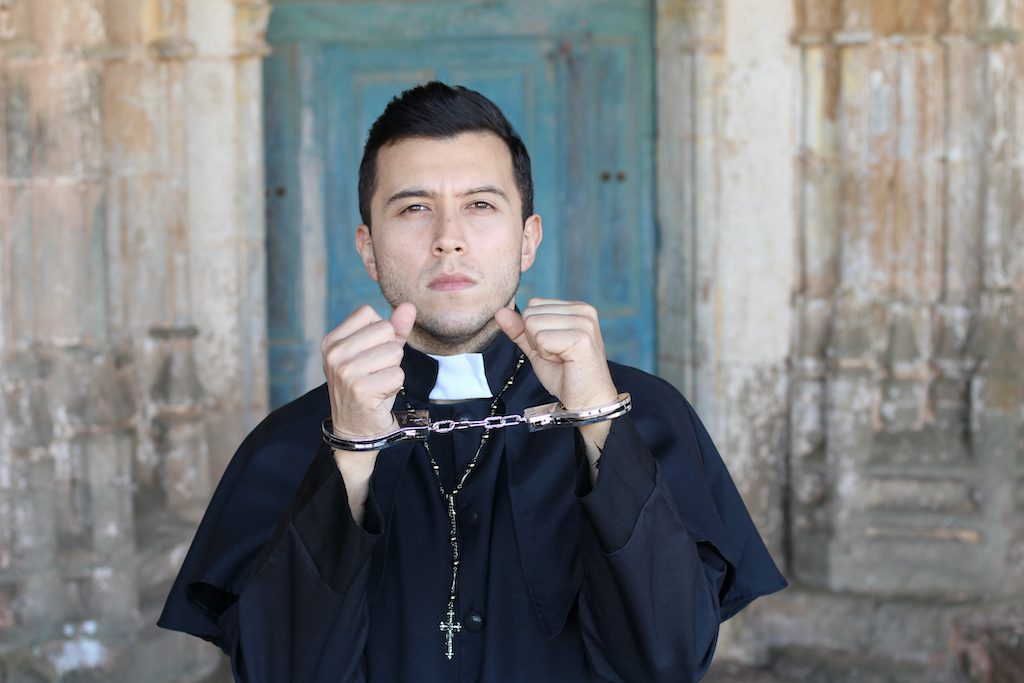 Handcuffed priest looking very upset