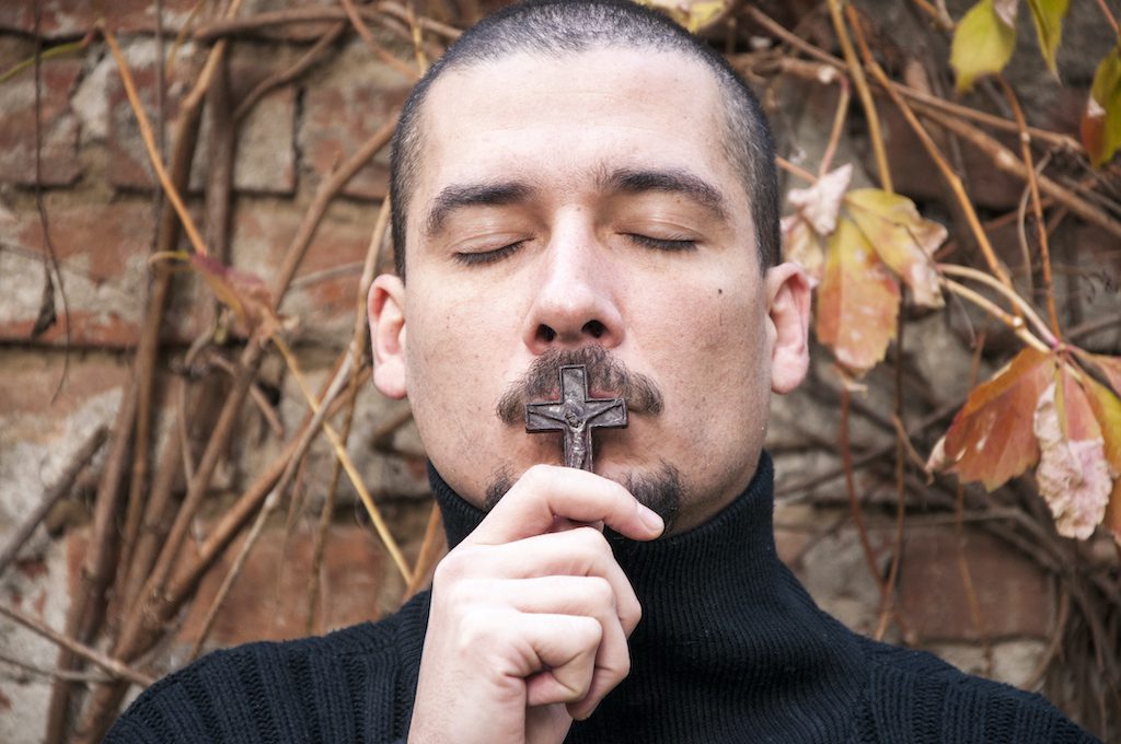 Close-Up Of Man With Eyes Closed Kissing Crucifix