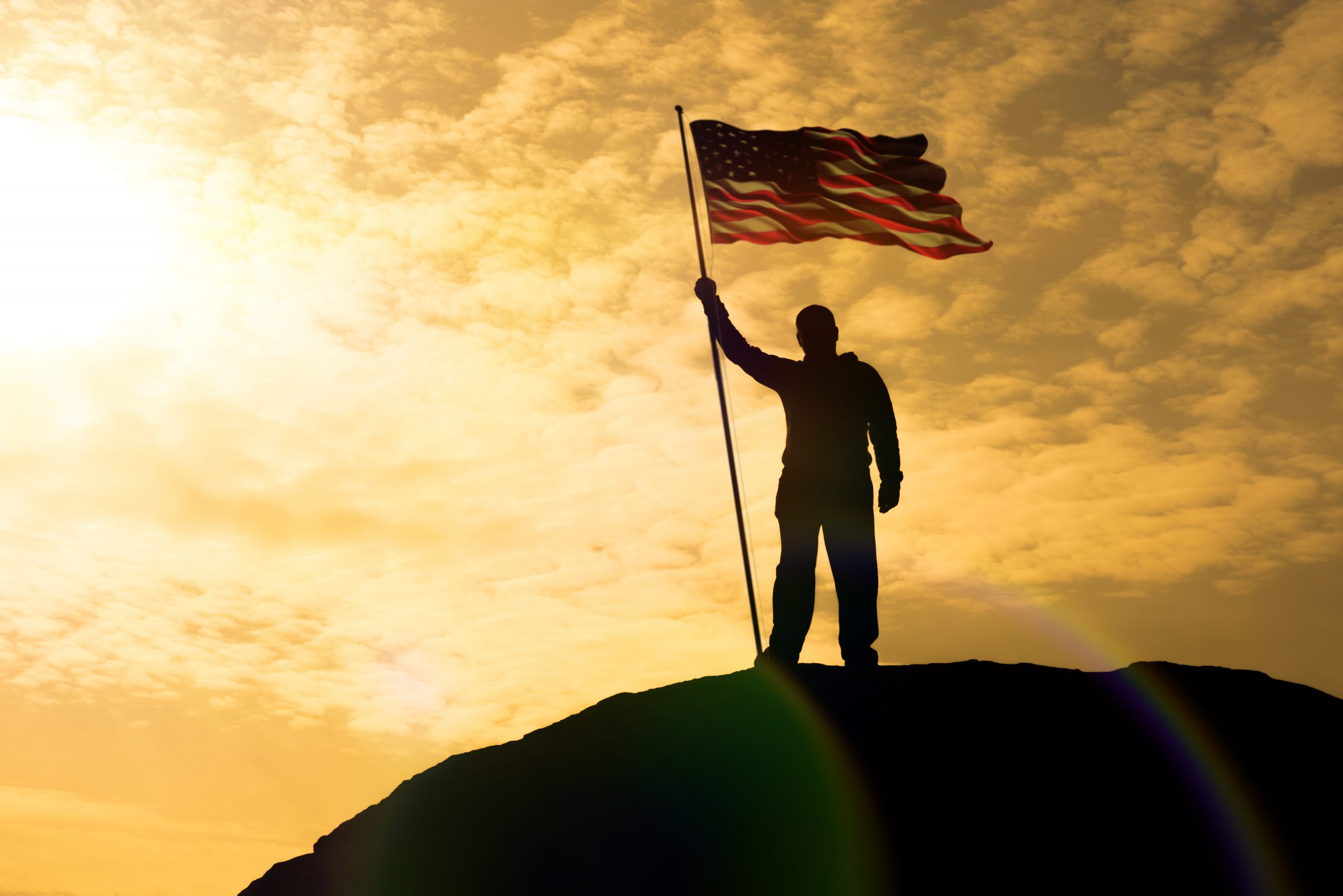 Silhouette,Of,Man,Holding,Us,Flag,American,On,The,Mountain.