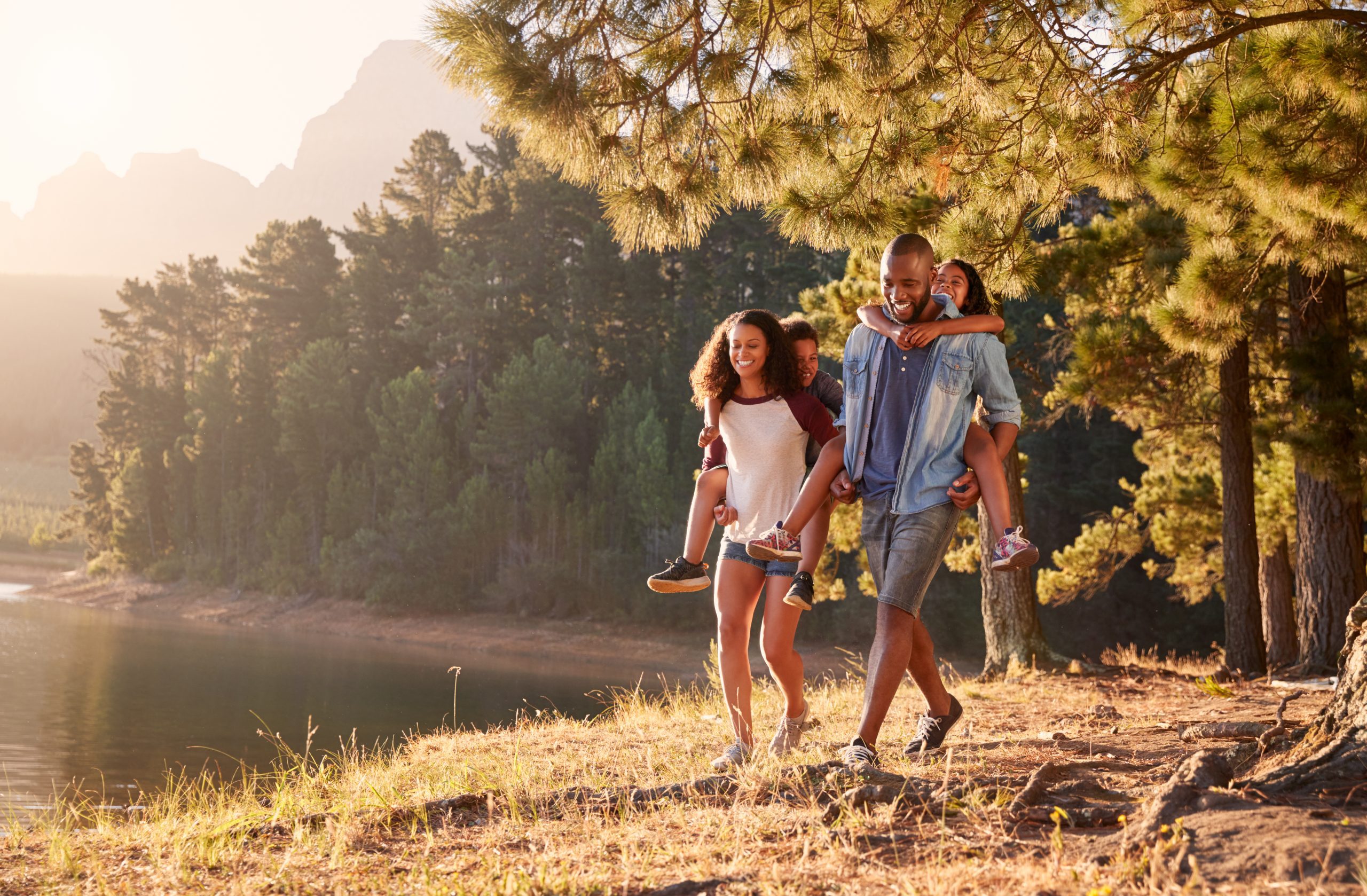 Parents,Giving,Children,Piggyback,Rides,On,Walk,By,Lake