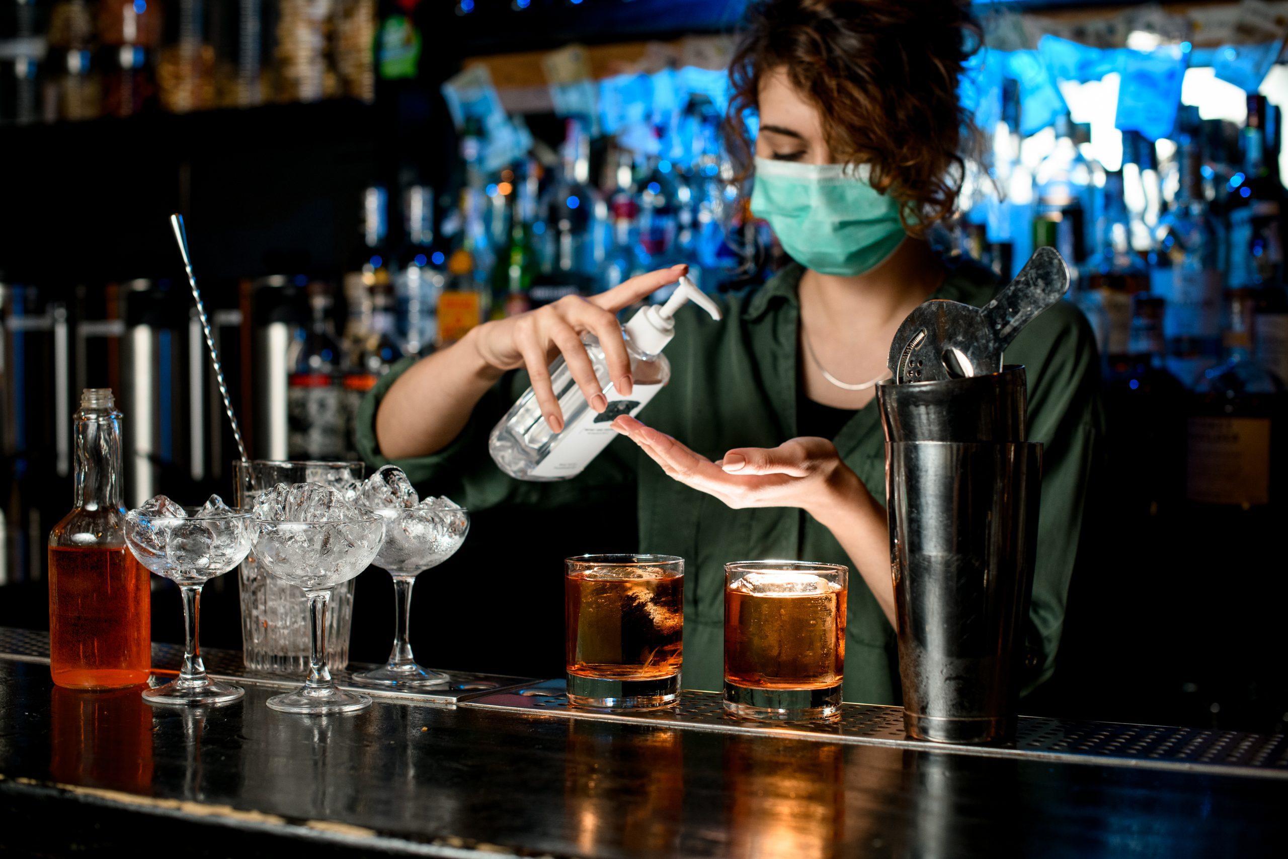 Woman,In,Medical,Mask,Treats,Her,Hands,With,Disinfector,Behind