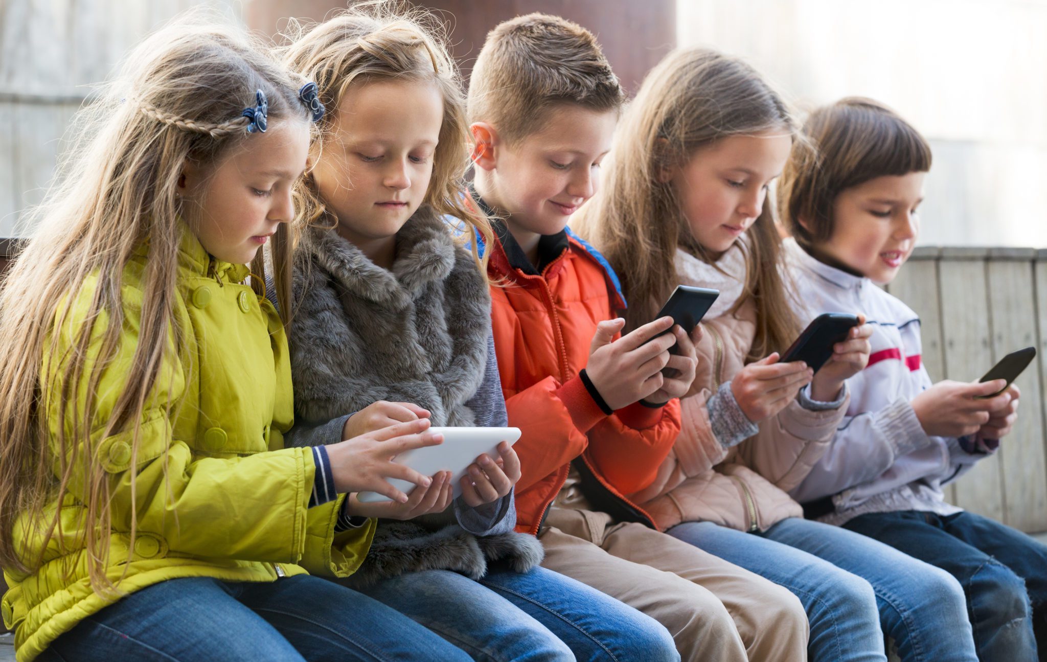 Ordinary,Kids,Sitting,With,Mobile,Devices,In,Street