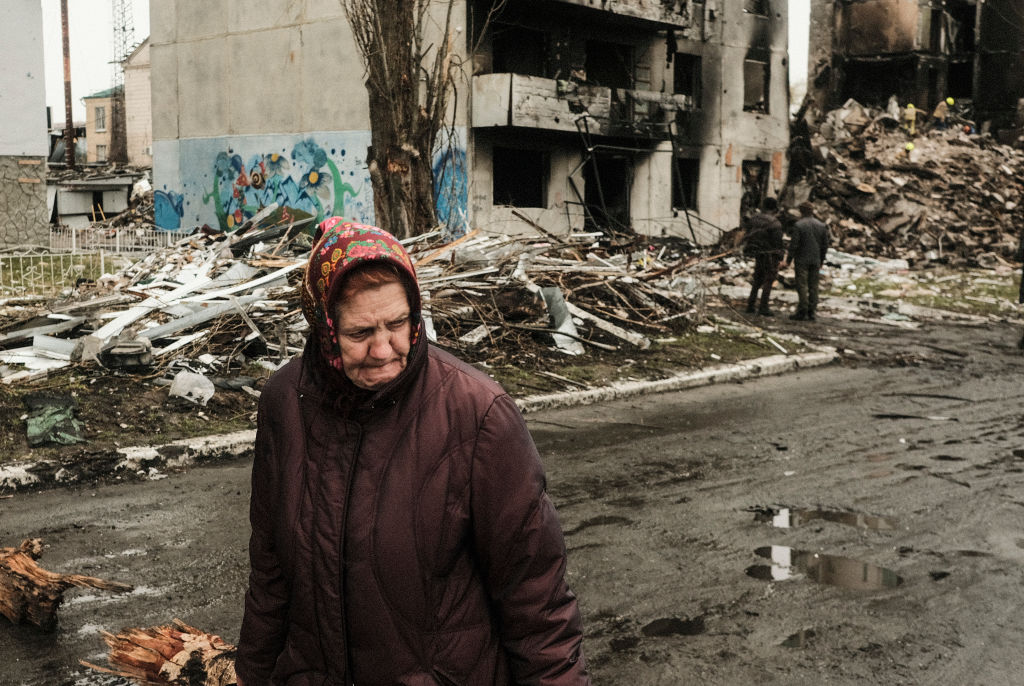 A woman walks past a destroyed apartment building in
