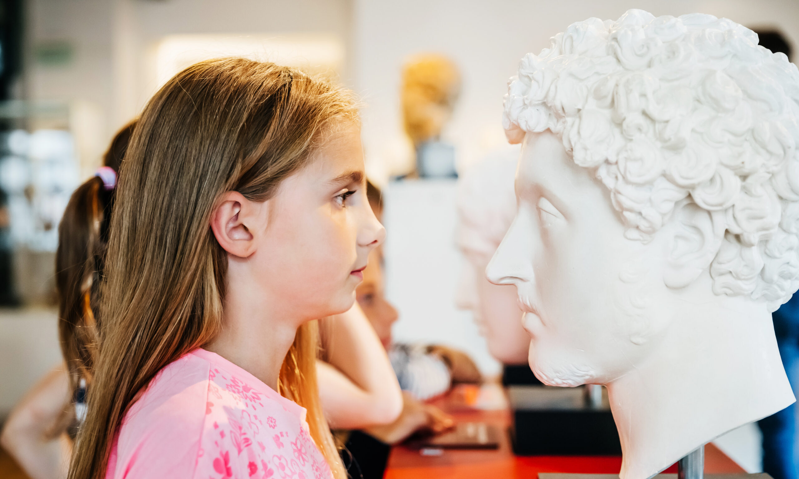Young Girl Looking Closely At Classical Bust In Museum