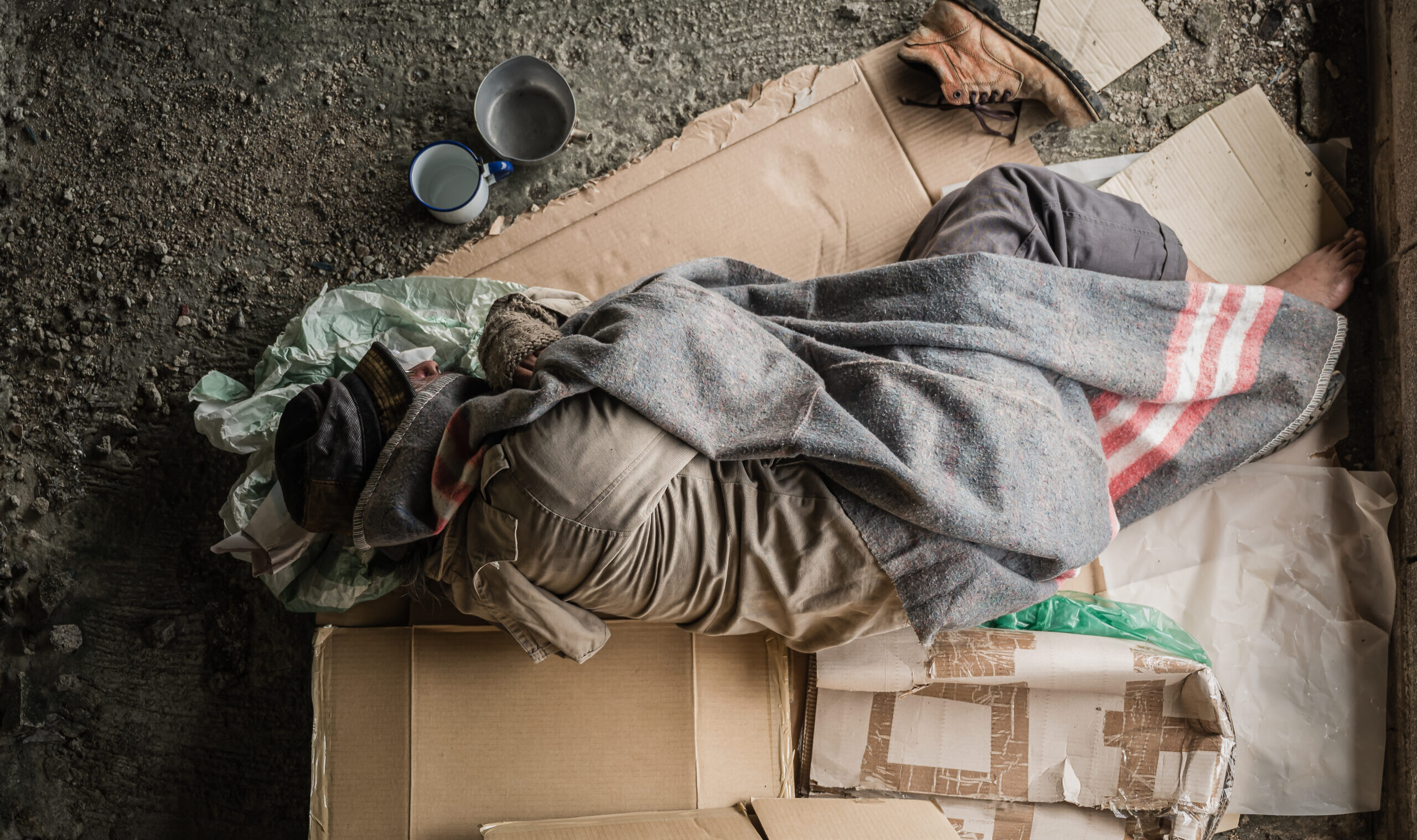 Old,Homeless,Man,Wearing,Sweater,And,Blanket,Sleeping,On,Cardboard