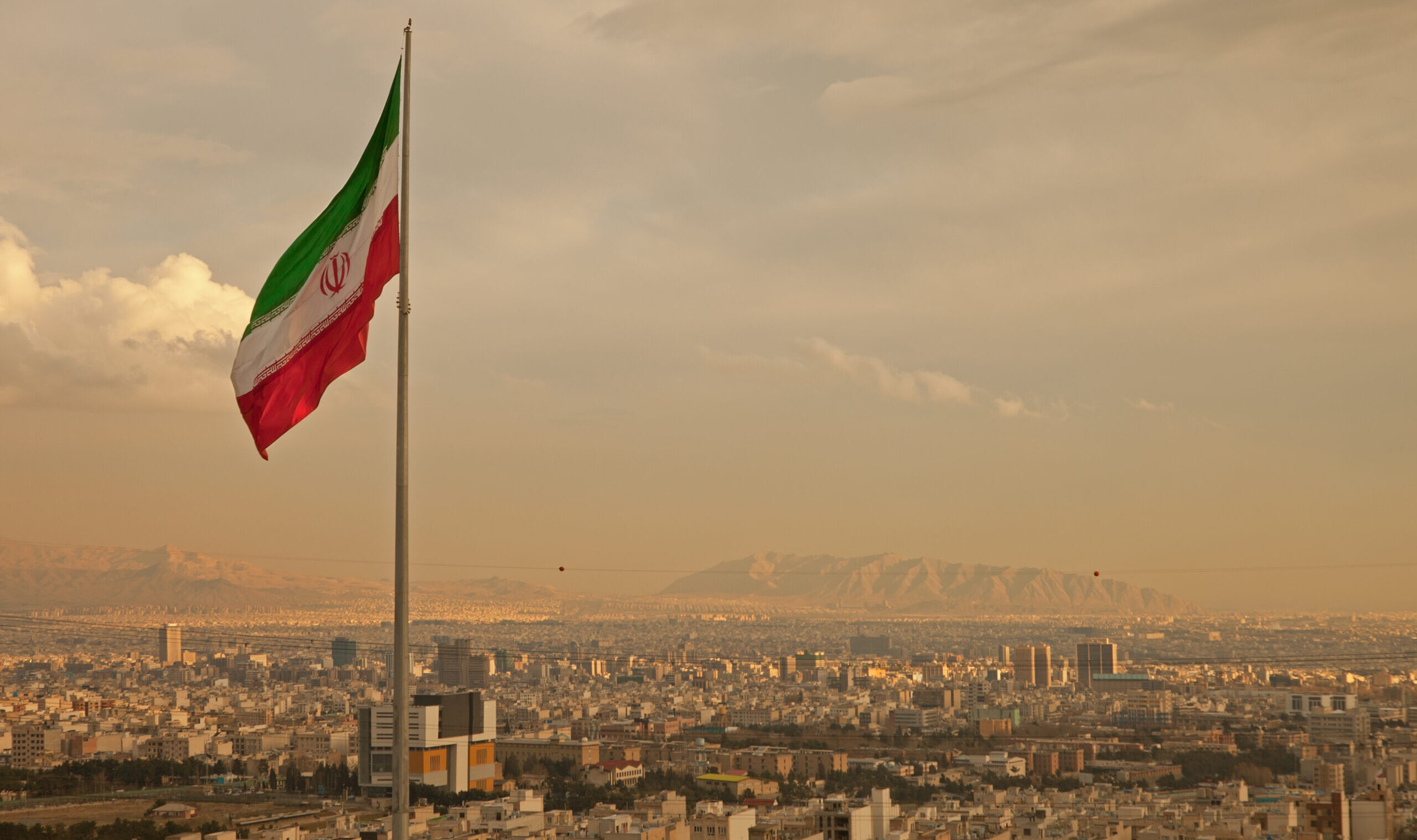 Iran,Flag,Waving,In,The,Wind,Above,Skyline,Of,Tehran